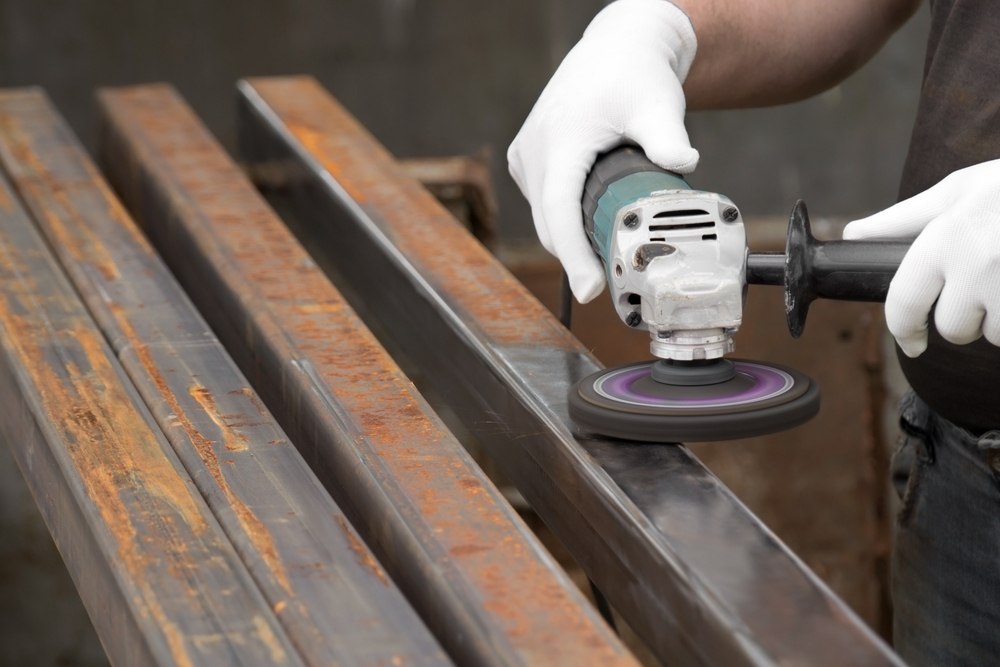 A person wearing white gloves sands a metal piece using a sander.